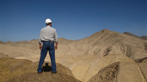 Miner on rock surveying landscape, rear view